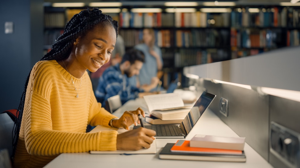 University Library: Gifted Black Girl uses Laptop, Writes Notes for the Paper, Essay, Study for Class Assignment. Diverse Multi-Ethnic Group of Students Learning, Studying for Exams, Talk in College