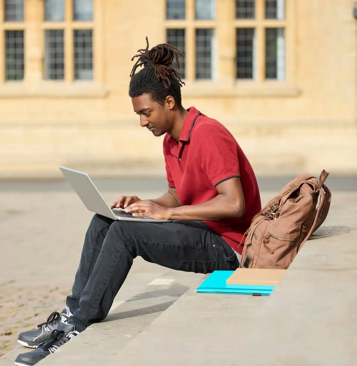 Male Student Working On Laptop Sitting On StepsOutside University Building In Oxford UK